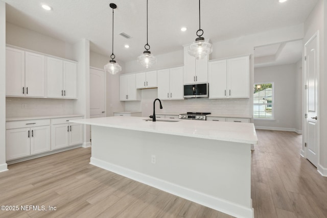 kitchen featuring sink, white cabinetry, stainless steel appliances, and an island with sink