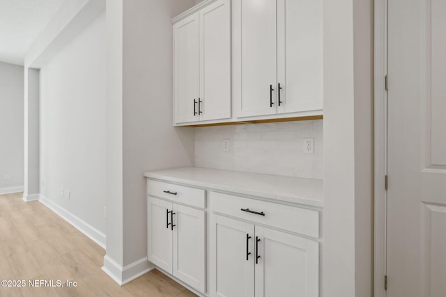 bar featuring decorative backsplash, light wood-type flooring, and white cabinetry