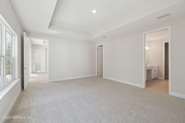 unfurnished bedroom with a raised ceiling, ensuite bath, and light colored carpet