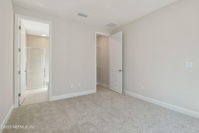 unfurnished bedroom featuring light carpet, a walk in closet, and ensuite bath