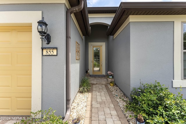 view of exterior entry with an attached garage and stucco siding