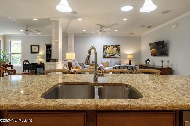 kitchen with ornate columns, ceiling fan, sink, light stone counters, and crown molding