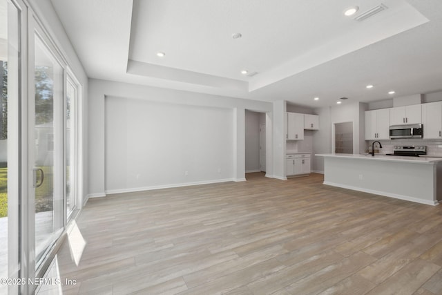 unfurnished living room with a tray ceiling, light hardwood / wood-style flooring, and sink