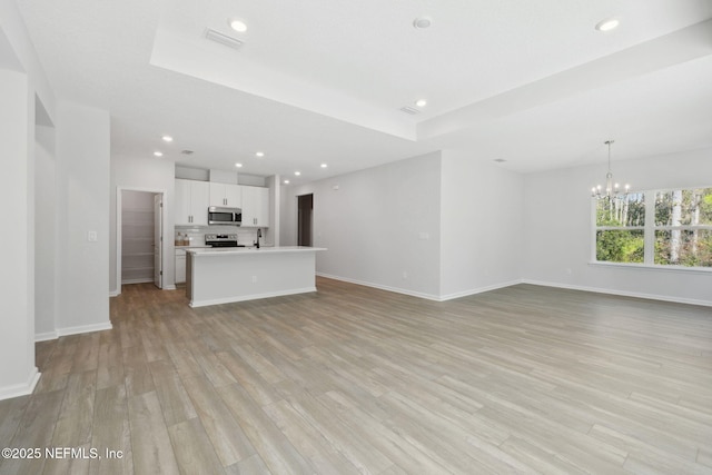 unfurnished living room with a chandelier and light wood-type flooring