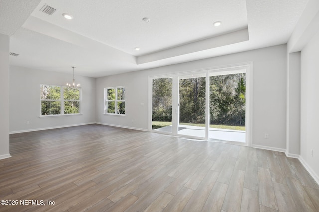 unfurnished living room featuring light wood-type flooring, a tray ceiling, plenty of natural light, and a notable chandelier