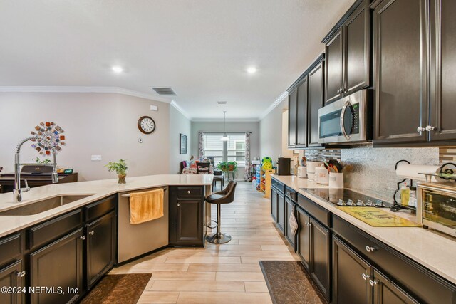 kitchen with crown molding, light wood-type flooring, stainless steel appliances, pendant lighting, and sink