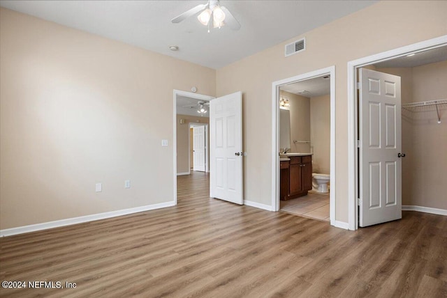 unfurnished bedroom featuring connected bathroom, ceiling fan, hardwood / wood-style floors, a walk in closet, and a closet