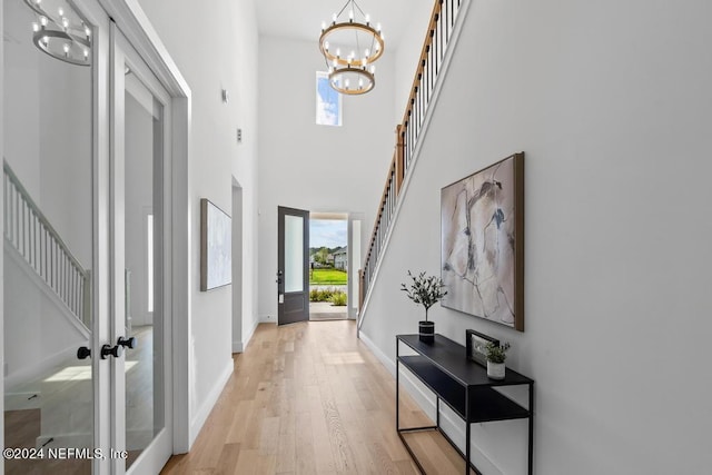 interior space featuring light wood-type flooring, french doors, a notable chandelier, and a towering ceiling