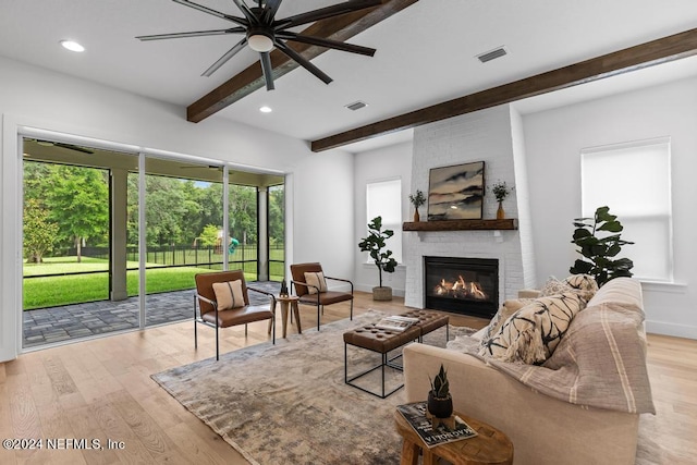 living room featuring ceiling fan, brick wall, beam ceiling, light hardwood / wood-style floors, and a brick fireplace