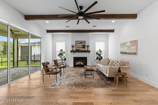 living room with beamed ceiling, a large fireplace, light wood-type flooring, and ceiling fan