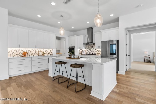 kitchen featuring white cabinets, decorative backsplash, an island with sink, wall chimney exhaust hood, and light carpet