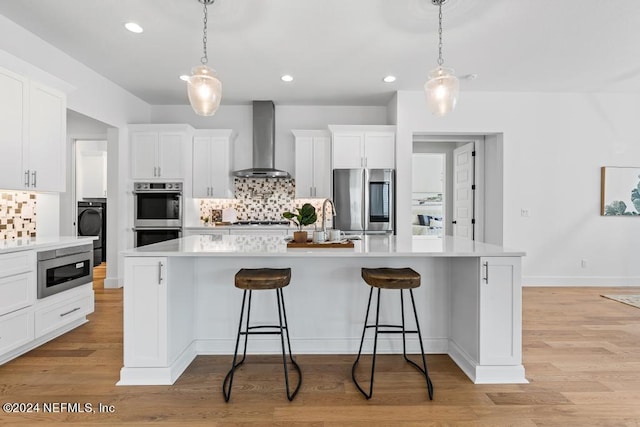 kitchen with decorative backsplash, appliances with stainless steel finishes, hanging light fixtures, and wall chimney exhaust hood