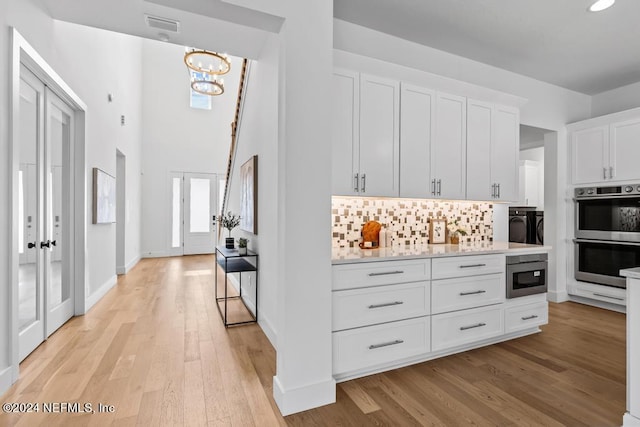 kitchen with white cabinetry, tasteful backsplash, light wood-type flooring, a high ceiling, and stainless steel double oven