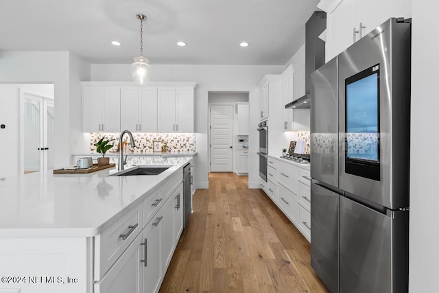 kitchen featuring stainless steel appliances, wall chimney range hood, decorative backsplash, light wood-type flooring, and white cabinetry