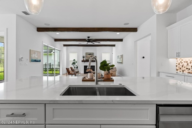 kitchen featuring decorative backsplash, white cabinetry, beamed ceiling, and sink