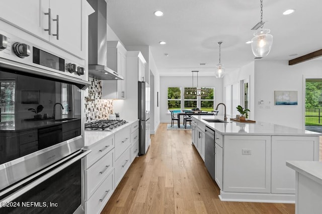 kitchen featuring tasteful backsplash, wall chimney range hood, light hardwood / wood-style floors, appliances with stainless steel finishes, and decorative light fixtures