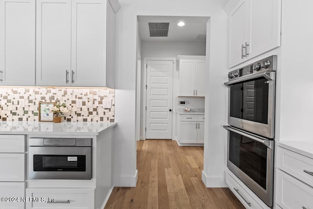 kitchen with double oven, backsplash, white cabinets, and light wood-type flooring