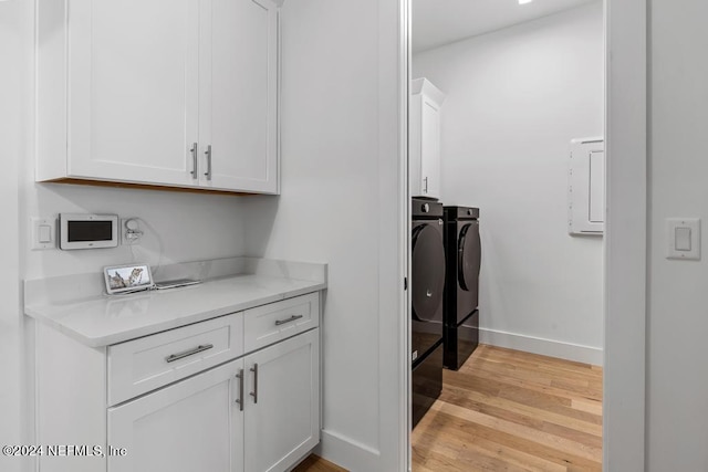 clothes washing area with cabinets, light wood-type flooring, washer and dryer, and electric panel