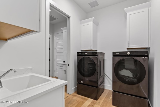 clothes washing area with cabinets, washing machine and dryer, sink, and light wood-type flooring