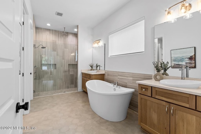 bathroom featuring plus walk in shower, tile patterned flooring, tile walls, and double sink vanity