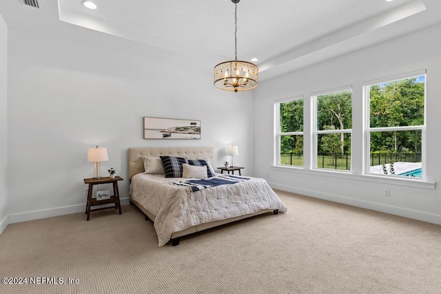 carpeted bedroom featuring a raised ceiling and a chandelier