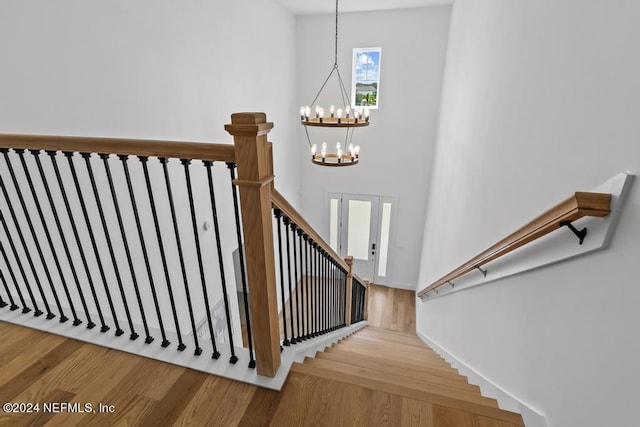 stairs featuring a notable chandelier, wood-type flooring, and a high ceiling