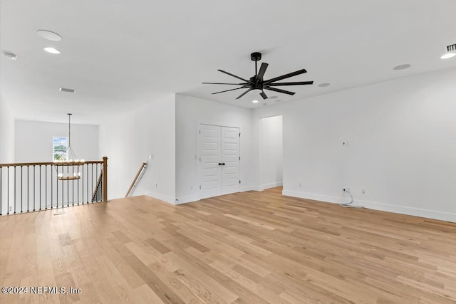 empty room with ceiling fan with notable chandelier and light hardwood / wood-style flooring