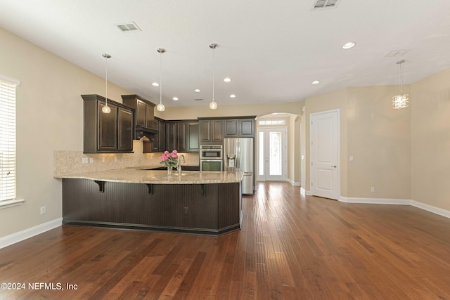 kitchen featuring tasteful backsplash, kitchen peninsula, hanging light fixtures, a breakfast bar, and appliances with stainless steel finishes