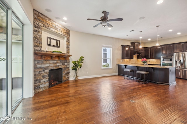 kitchen with hanging light fixtures, stainless steel appliances, a kitchen bar, dark brown cabinets, and a stone fireplace