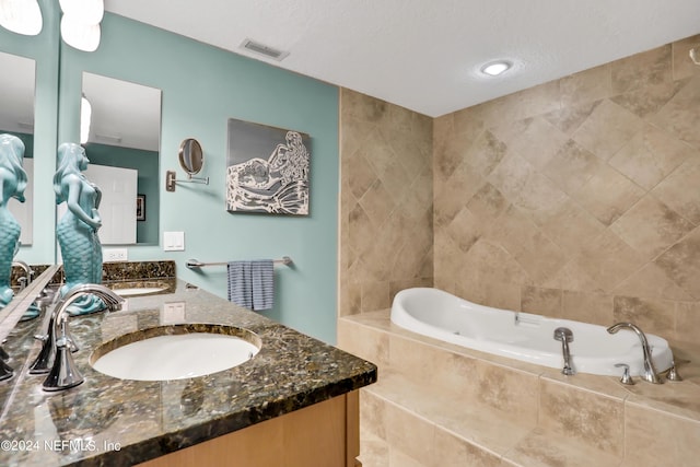 bathroom featuring vanity, a relaxing tiled tub, and a textured ceiling