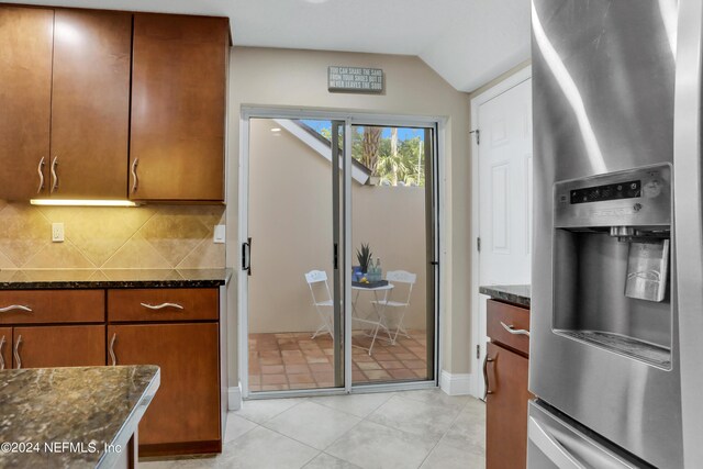 kitchen with stainless steel refrigerator with ice dispenser, backsplash, and dark stone counters