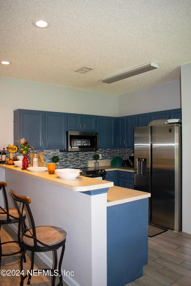 kitchen with blue cabinetry, stainless steel appliances, kitchen peninsula, and a breakfast bar area