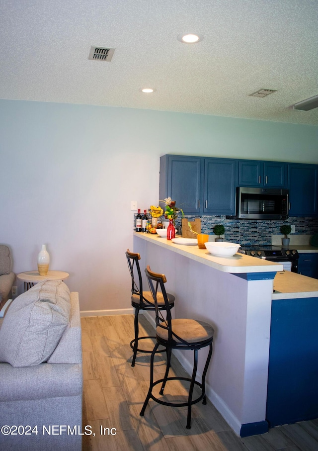 kitchen with kitchen peninsula, blue cabinets, backsplash, and a breakfast bar area