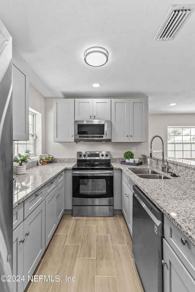 kitchen with light stone countertops, appliances with stainless steel finishes, gray cabinetry, and sink