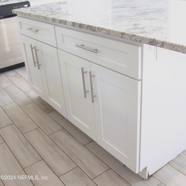 interior details featuring white cabinets, stainless steel dishwasher, and light stone countertops