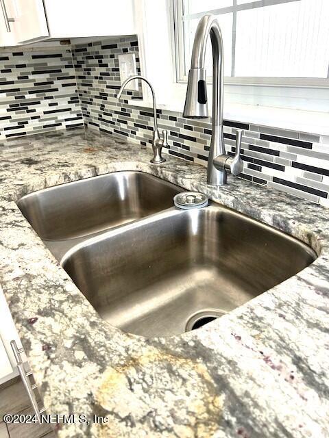 interior details with decorative backsplash, white cabinetry, sink, and stone countertops