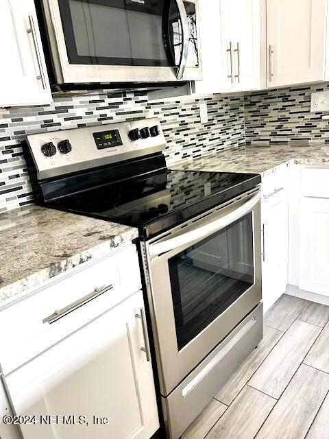 kitchen featuring light stone countertops, white cabinetry, and electric stove