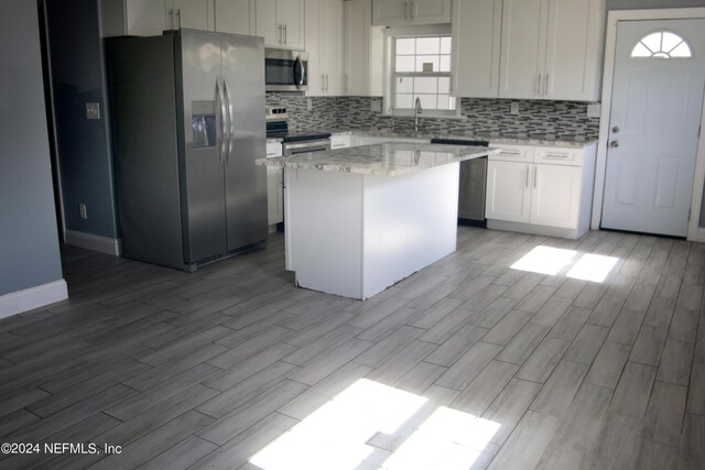 kitchen with a center island, white cabinets, light stone countertops, light hardwood / wood-style floors, and stainless steel appliances