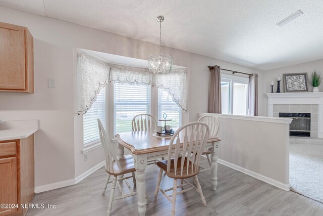 dining area featuring a tile fireplace, light hardwood / wood-style flooring, a textured ceiling, and a notable chandelier