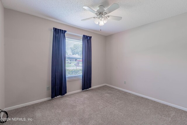 empty room with ceiling fan, light colored carpet, and a textured ceiling