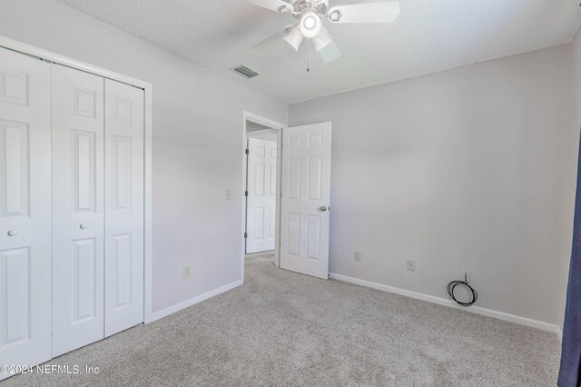 unfurnished bedroom featuring a textured ceiling, ceiling fan, light carpet, and a closet