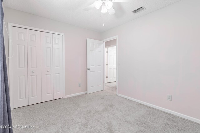 unfurnished bedroom with a textured ceiling, a closet, ceiling fan, and light colored carpet