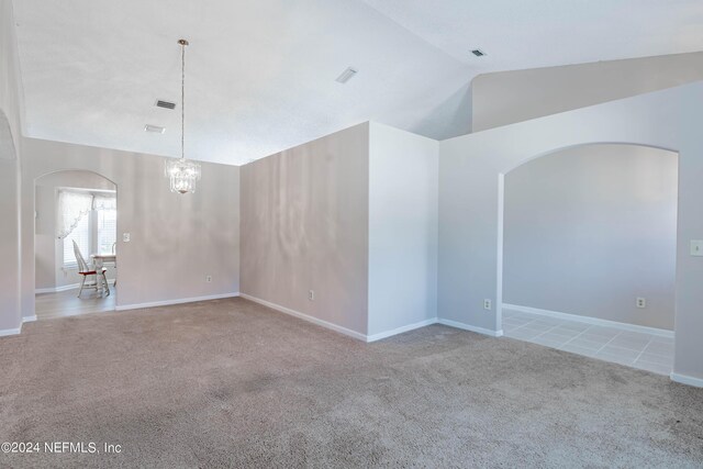 empty room featuring a chandelier, light colored carpet, and vaulted ceiling