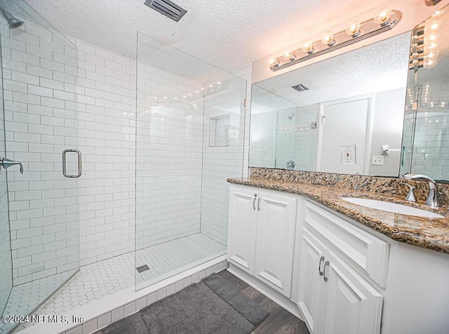 bathroom featuring a textured ceiling, a shower with door, and vanity