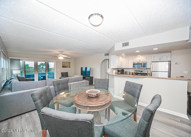 dining area featuring ceiling fan, light wood-type flooring, and a textured ceiling