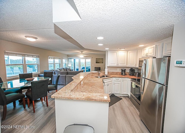 kitchen featuring white cabinetry, ceiling fan, kitchen peninsula, light stone countertops, and appliances with stainless steel finishes