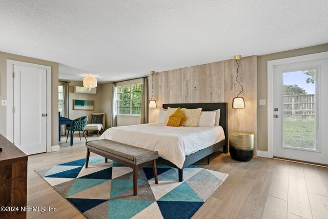 bedroom featuring a wall mounted air conditioner, a textured ceiling, light wood-type flooring, and multiple windows