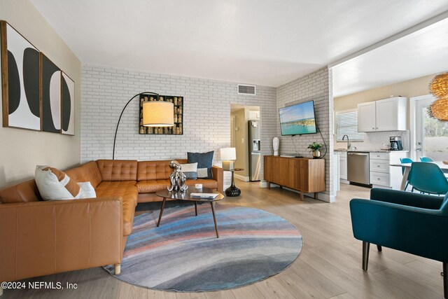 living room featuring sink, light hardwood / wood-style floors, and brick wall