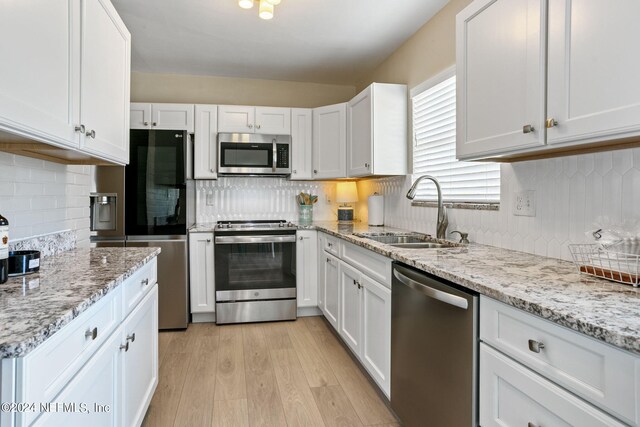 kitchen featuring tasteful backsplash, light wood-type flooring, sink, white cabinetry, and appliances with stainless steel finishes