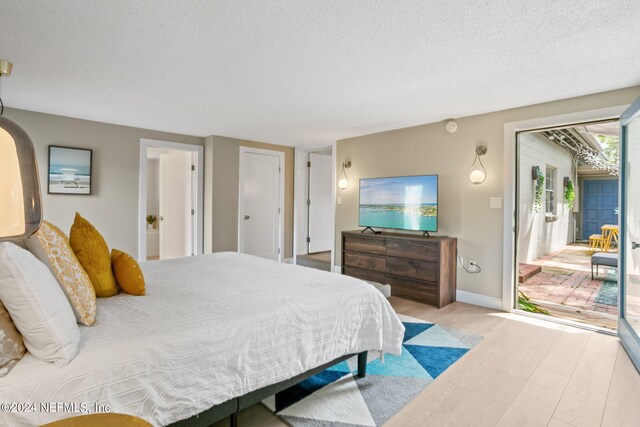 bedroom with light wood-type flooring, a textured ceiling, and multiple windows